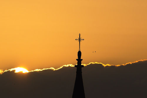 photo du soleil caché par un nuage et deux clochers d'église